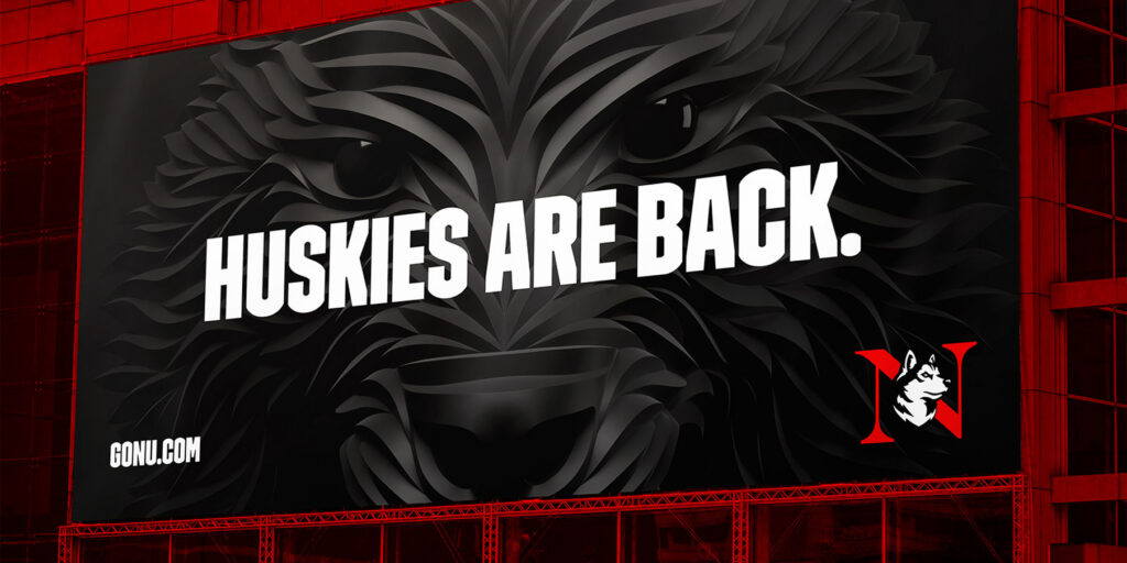 A billboard with a stylized black husky face, large white text reading "HUSKIES ARE BACK," the Northeastern University logo, and the website GoNU.com.