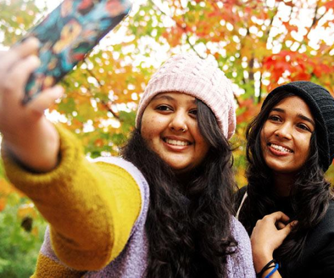 Students taking a selfie outdoors in the fall foliage