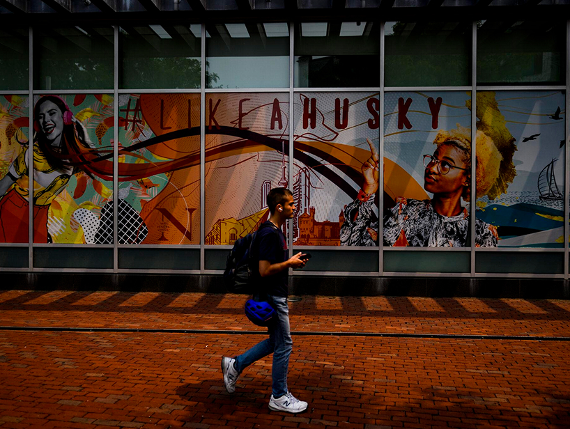 Student walking on campus past a public art mural