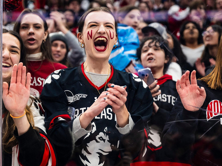 Excited sport fans wearing Northeastern University Husky branded clothing cheering and clapping