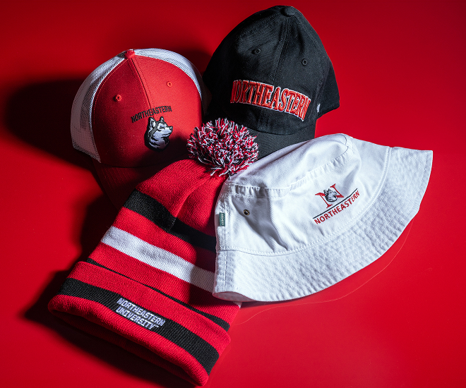 Four hats with Northeastern logos on a red background