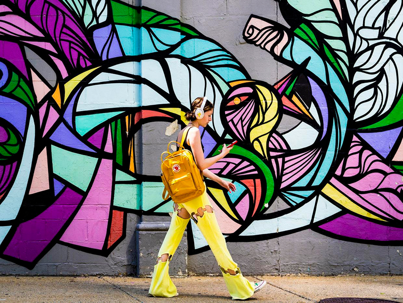 A person bright yellow trousers walks past a colorful mural.