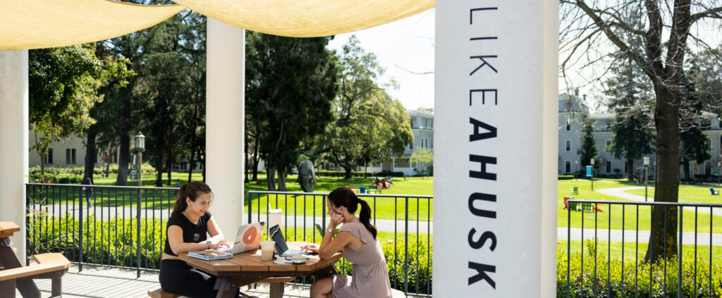 Two students sit outdoors at Suzanne Adams Plaza while they work on laptops and enjoy drinks from the Tea Shop at Northeastern University's Oakland campus